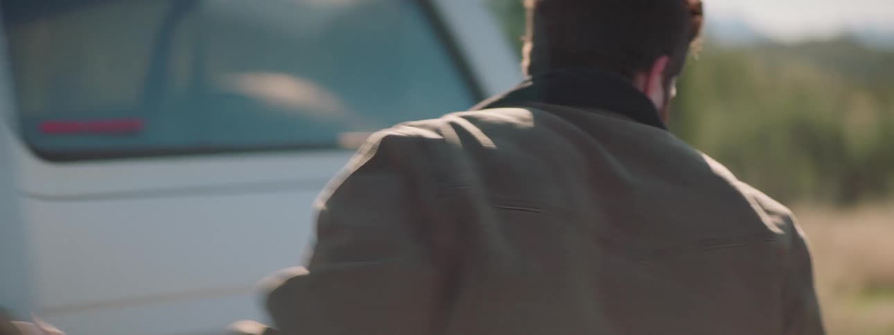 A man standing on a road throws his hat on the ground and then opens his truck door and then goes and picks up his hat