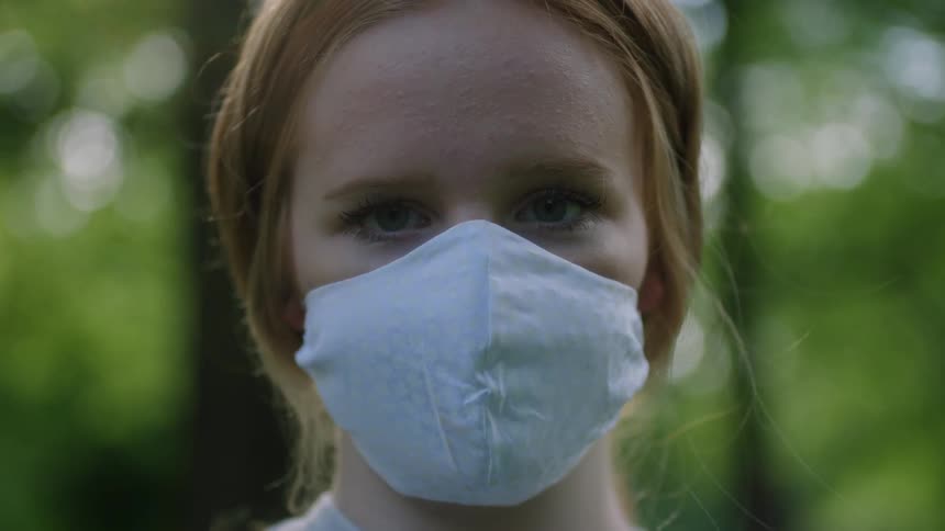 Blonde woman wearing face mask looks up to the camera while standing near a street