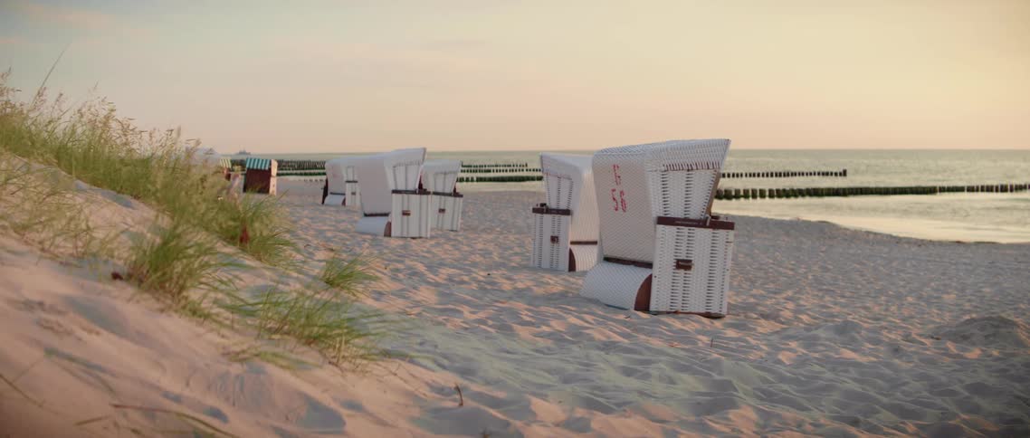 Surf crashes onto beach near small buildings and boxes lying near dune