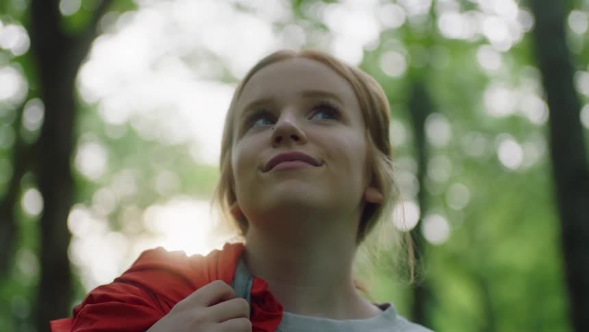 A teenage girl smiles while looking around in a forest