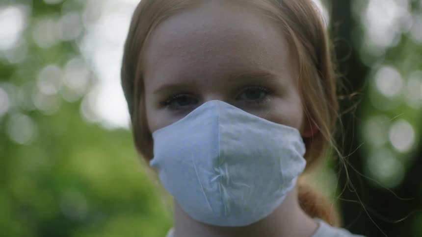 A woman wears a white protective mask she stands outsides in front of trees