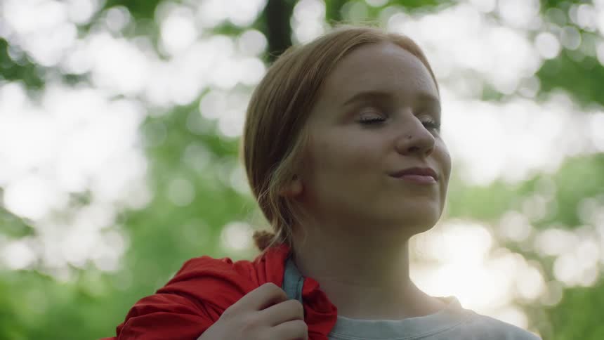 Young blonde woman looks at the camera and smiles in the forest at sunset