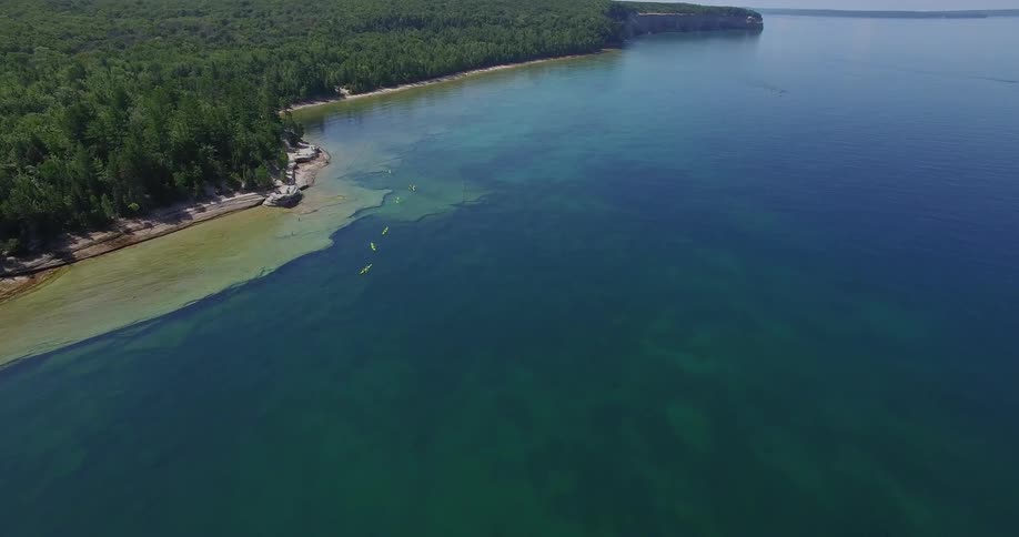 People in canoes paddle beside the forested shoreline