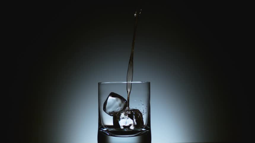 Liquor being poured over ice cubes inside a glass