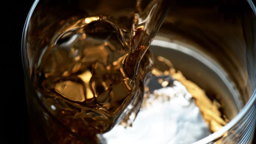 Amber alcohol flows into glass over ice cube