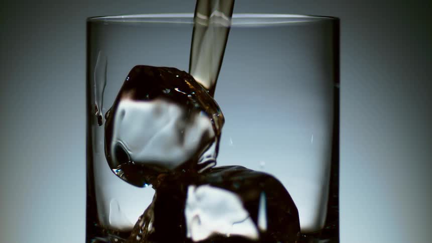 Alcohol pouring over ice in a cocktail glass