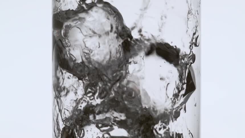 Soda is being poured into a glass with ice cubes