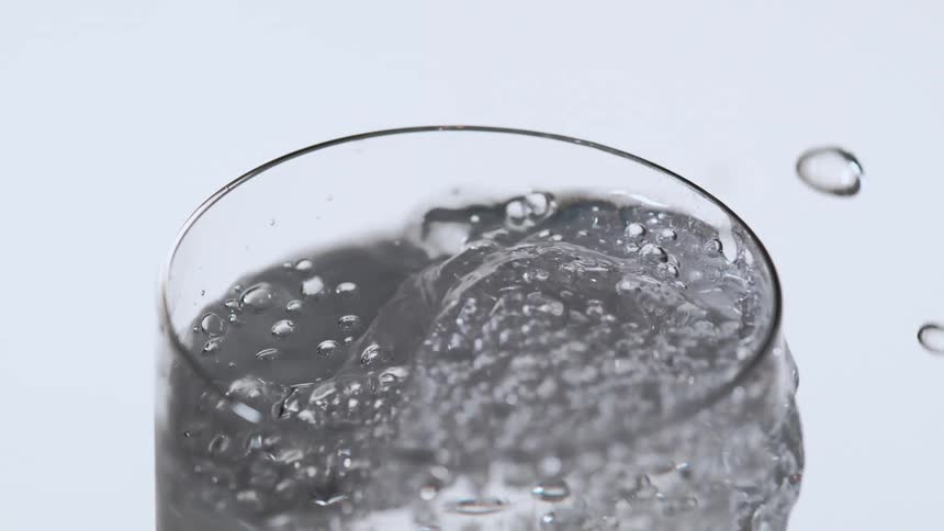 Ice drops into clear liquid splashing and creating bubbles