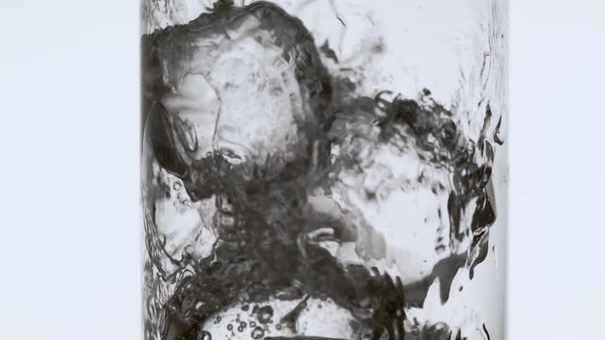 A beverage being poured in to a glass with ice