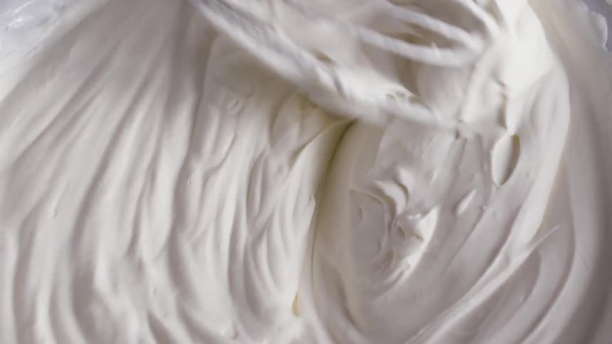 White cream inside a bowl being mixed with a metallic whisker