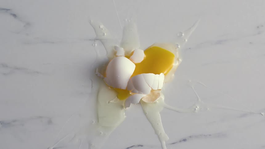 An egg falls and breaks on a marble surface