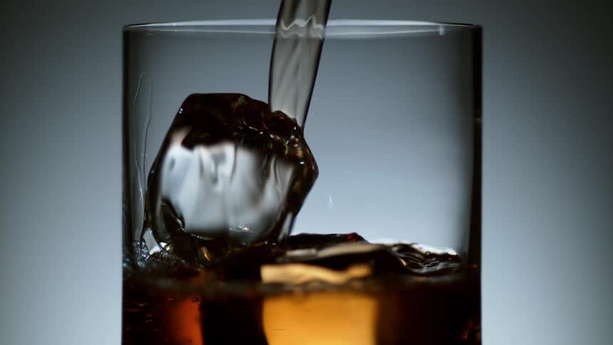 Liquor being poured into a glass with ice cubes