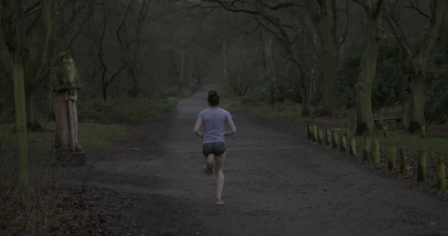 A woman runs down a path with woods on both sides