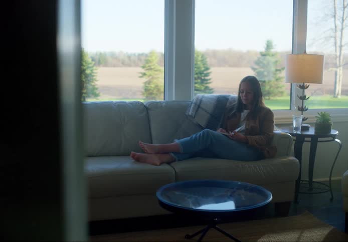 A barefoot woman sits on a sofa as she writes in notebook