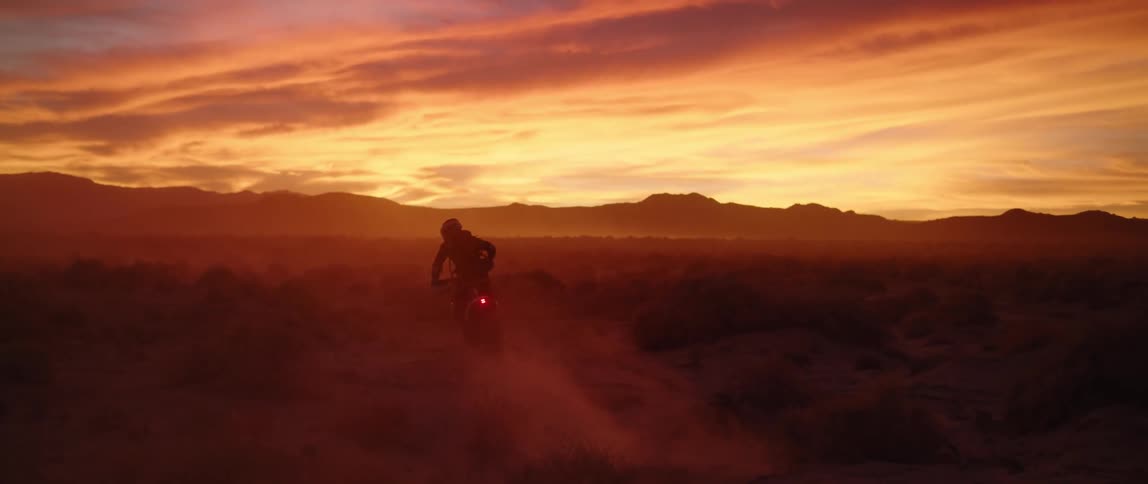 A person is riding a motorcycle into the horizon