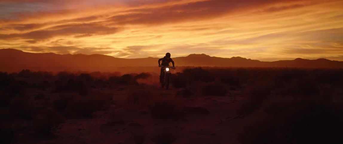 Person drives a motorcycle through the desert at sunset