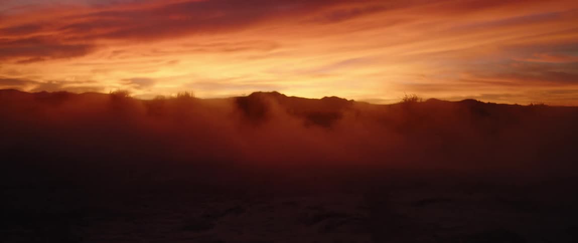 A person causes a dust cloud as he rides his dirt bike at sunset