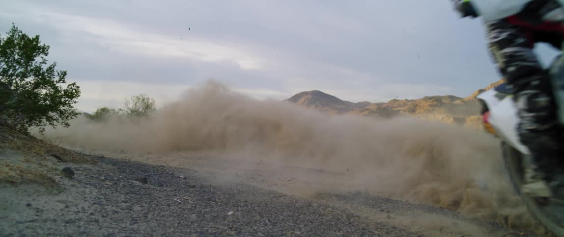 A person riding a motorbike through a gravel area
