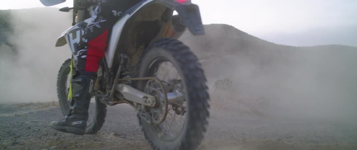 Motorcyclist rides on the dusty field near the mountains