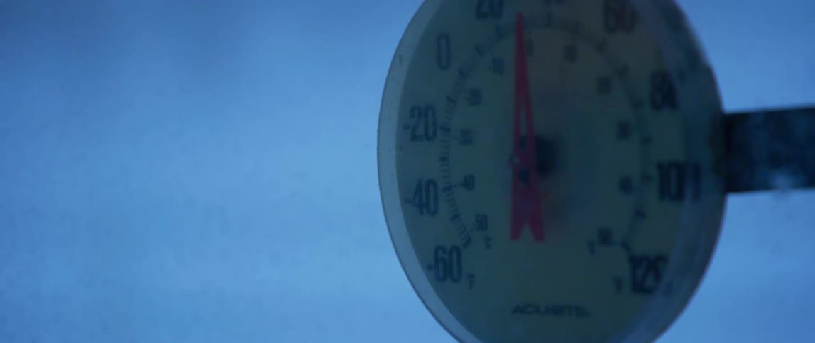 A winter storm blows in snow and wind against an outdoor thermometer