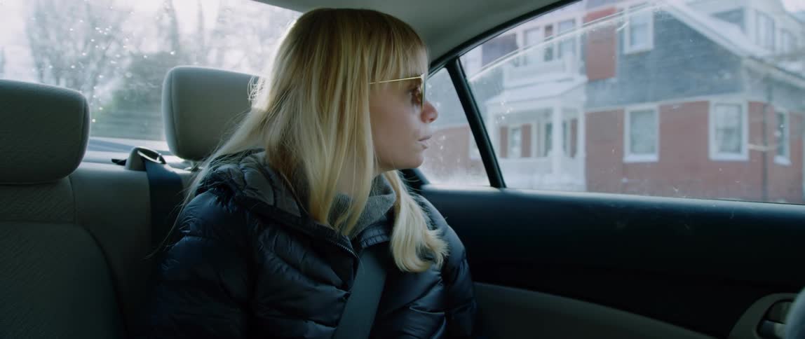 A woman in the back seat of a taxi looks up from her phone as the car slows down