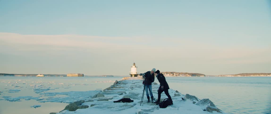 A photographer and her assistant work together to capture a wintery coastline photograph