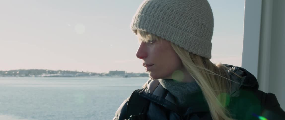 A woman stands on the bow of a ship and looks around at the wintery coastal views