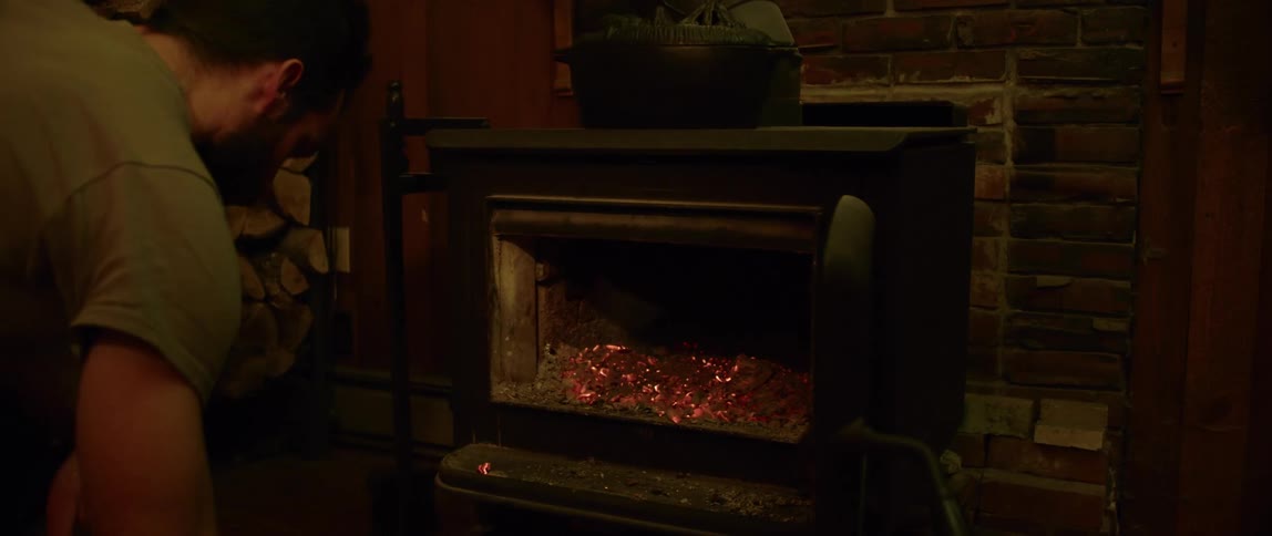 A man stokes hot coals in a wood stove before adding more wood to the fire