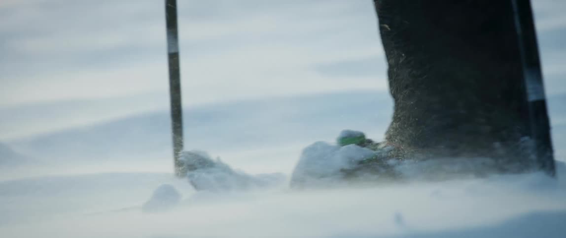 An outdoorsman snowshoes along a wintery terrain in windy conditions