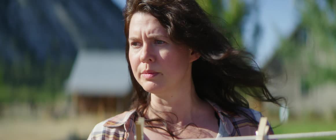 Woman hanging clothes outdoors on a windy day looks around nervously