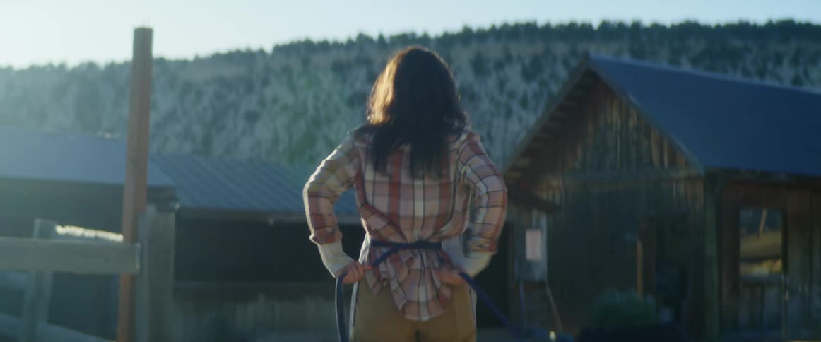 A woman ties an apron around her waist while walking to a barn in the country