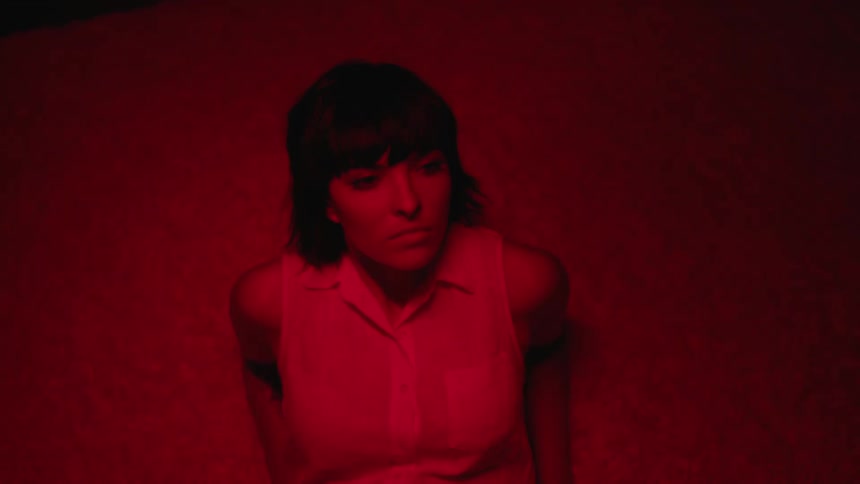 Woman laying over a rug projects shadows in the floor under a red swinging light in a dark room