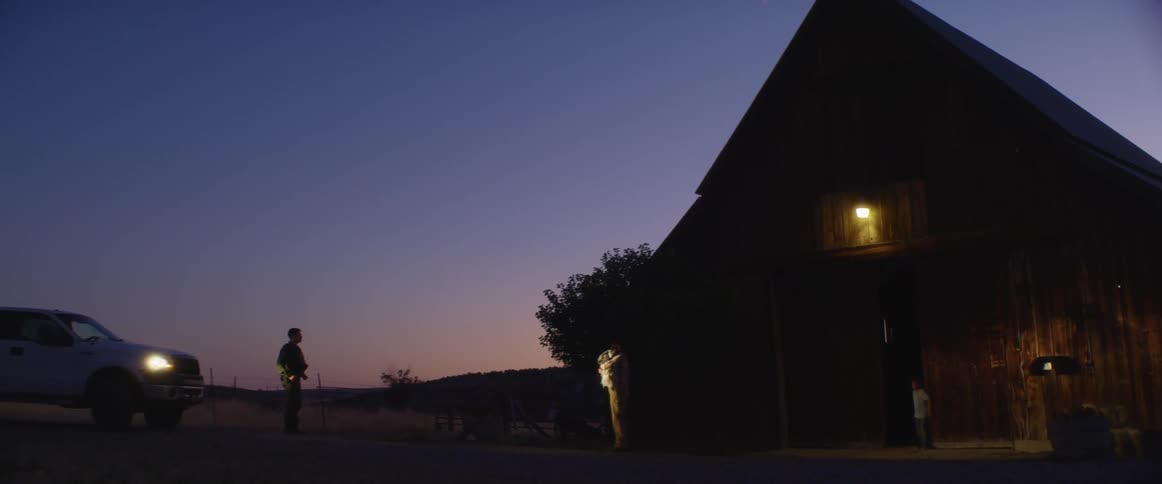 Two people have a conversation outside a barn at sunset