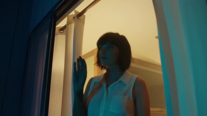 Woman walks to the window and looks outside the house at night