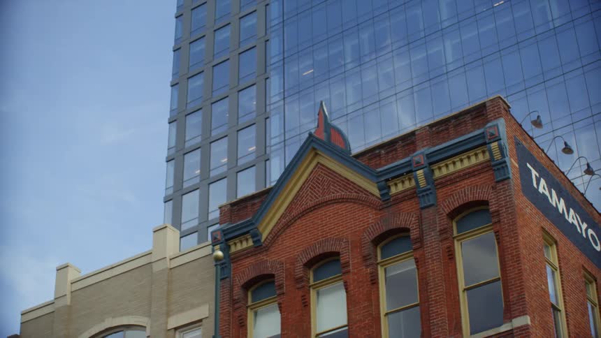Skyscraper towers over red bricked building with sign on the side