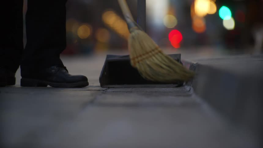A person sweeps the street with a small broom at sunset