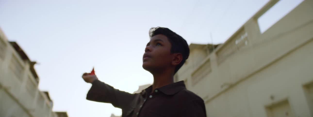 A young boy standing outside in a street holds a toy over his head like its flying