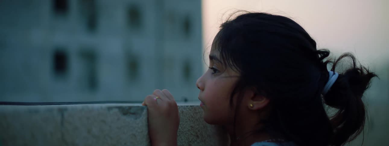 Little girl looks over the low wall of a balcony at sunset