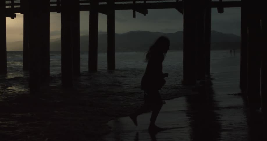 Person running from tidal waters under a pier