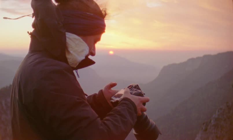 A person stands high in the mountains holding a camera to the horizon scenery
