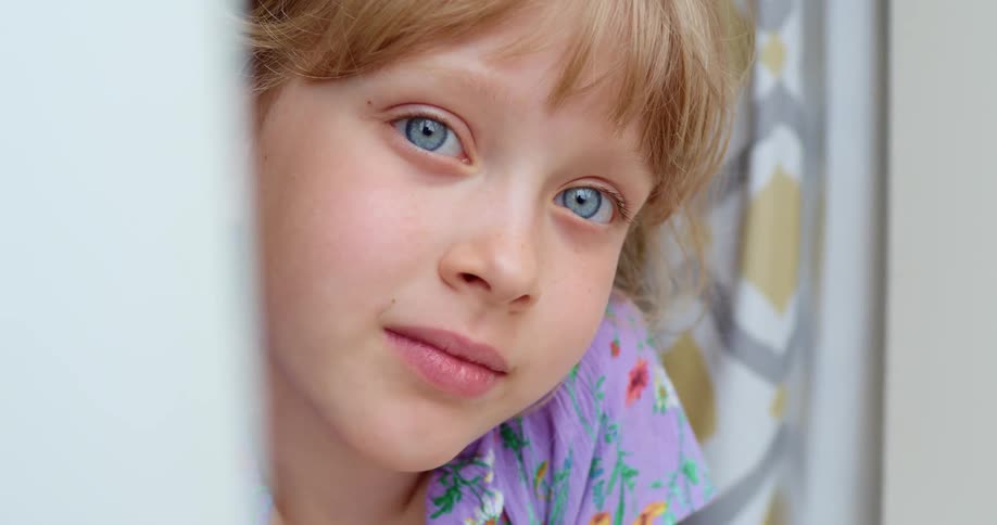 Blonde blue eyed girl leans against curtained opening
