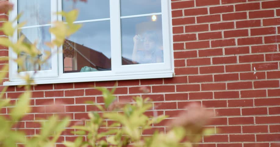 Child writes on glass of window inset in red brick wall