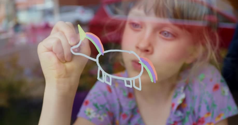 A young girl draws a unicorn on a window at her house