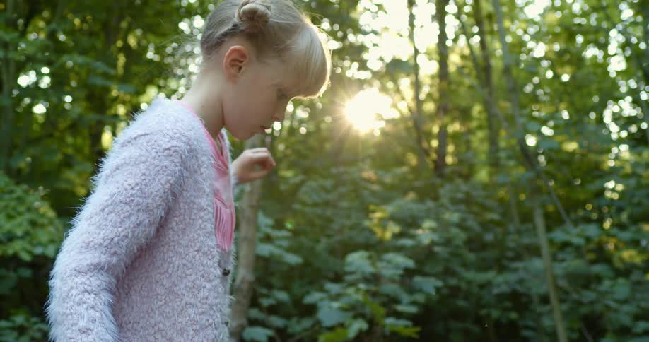 Blonde girl wearing a sweater plays in the forest at sunset