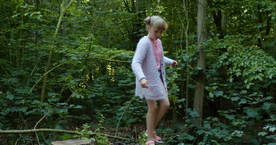 A young girl in a forest climbs up on a tree trunk and then walks across a stump and jumps off