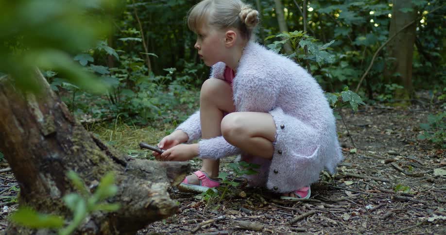 A girl crouches down with a stick in the forest