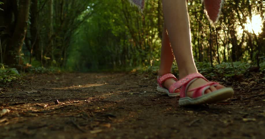A young girl hikes through a forest alone in pink sandals