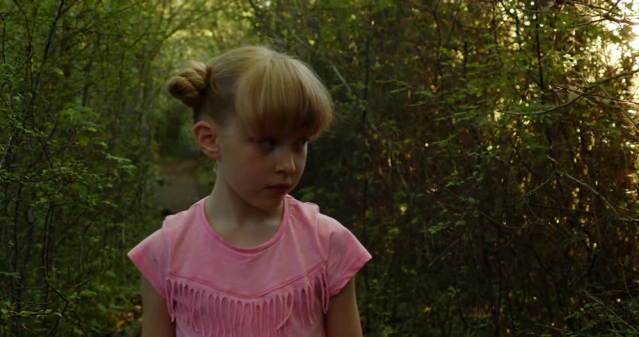 A young girl in a pink shirt walks alone in a forest on a sunny day