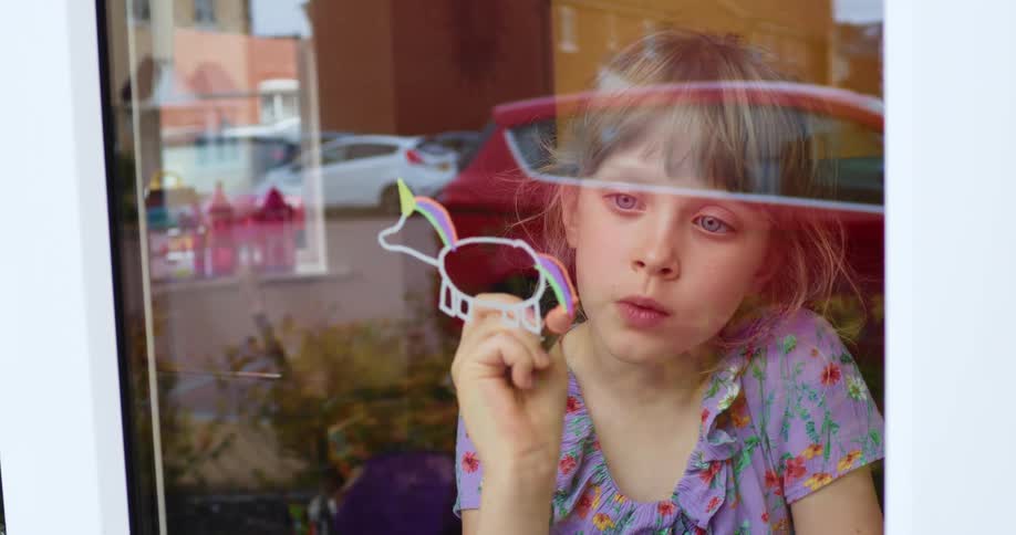 Girl drawing unicorns in the window at home