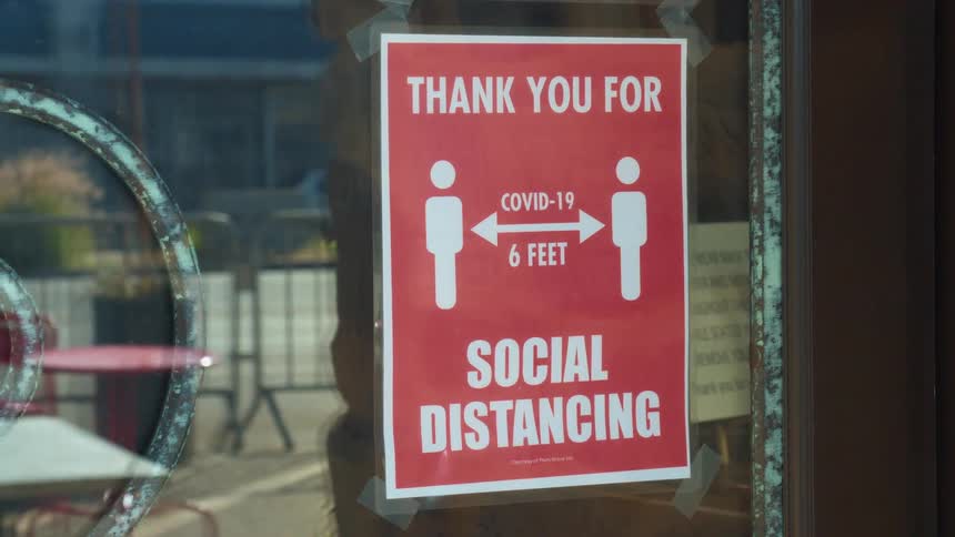 Social distancing sign hangs in a window as cars travel down a city street